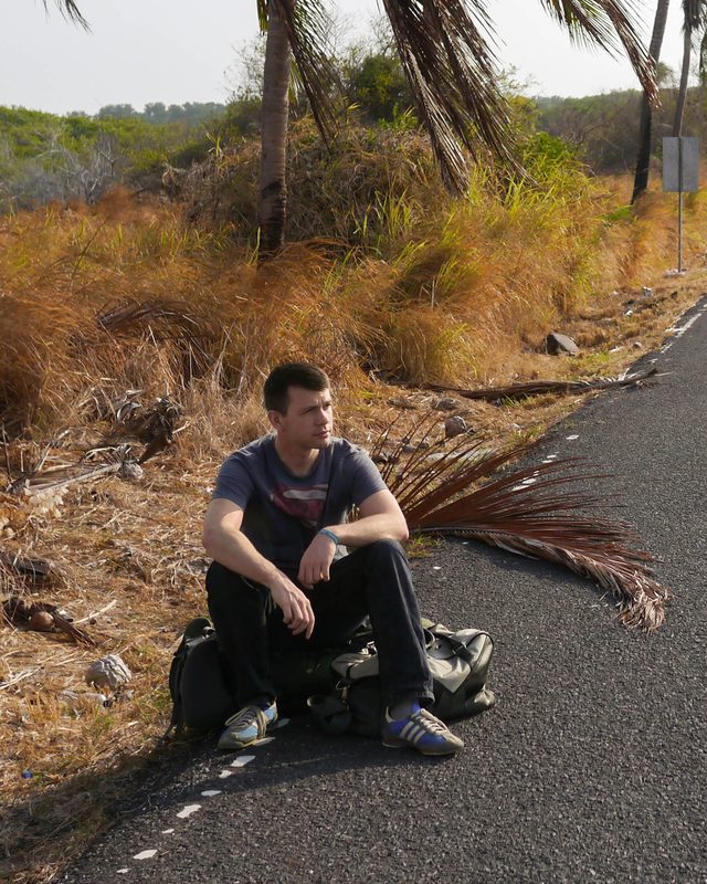 Thomas sitting on his backpack at the side of a road